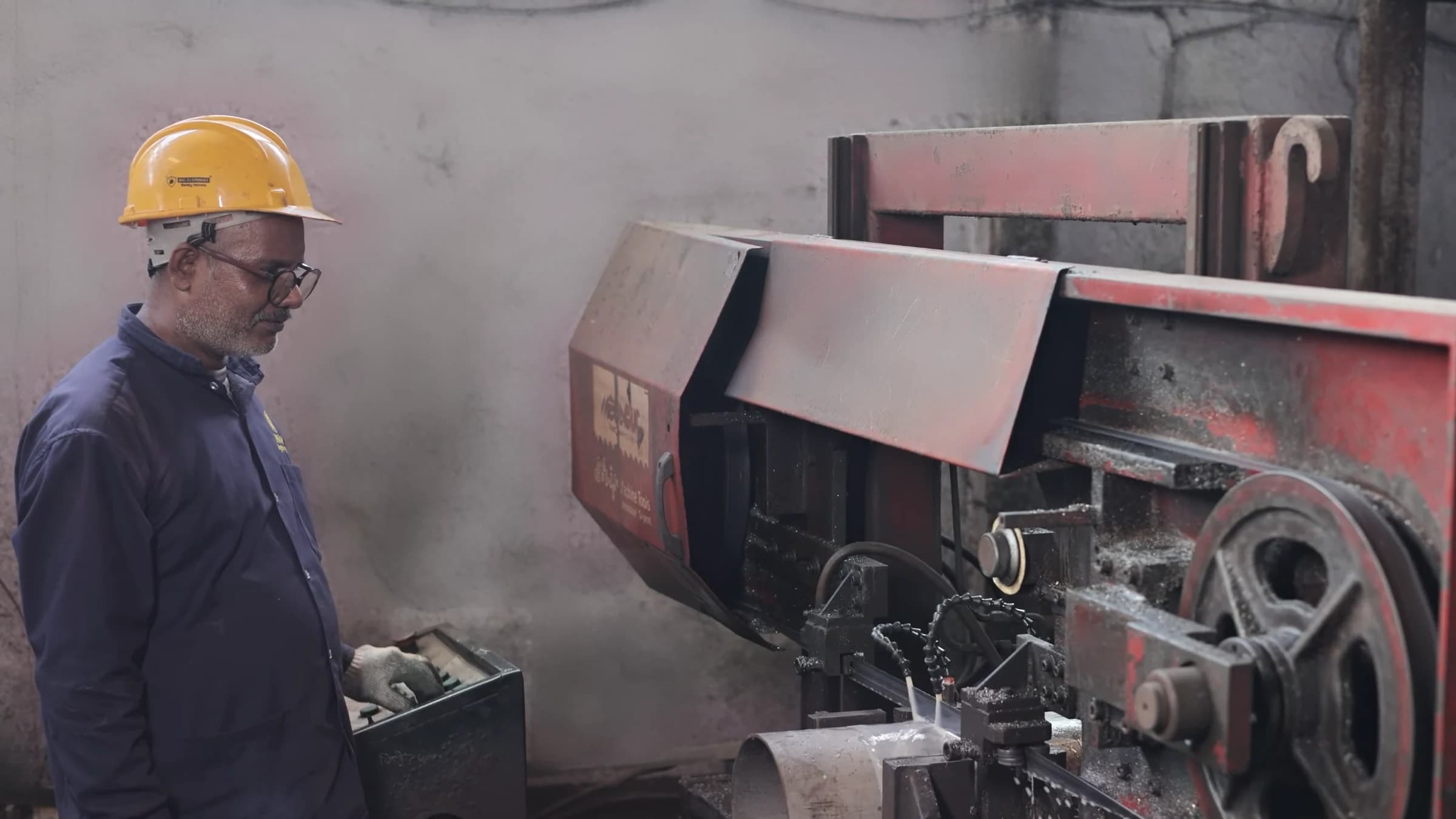 Operator in a safety helmet and gloves at the controls of a band saw