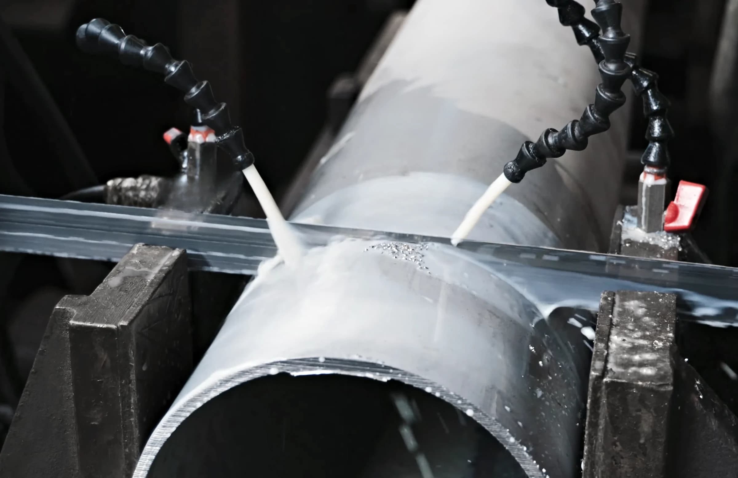 Band saw blade cutting through a stainless-steel pipe under two coolant jets