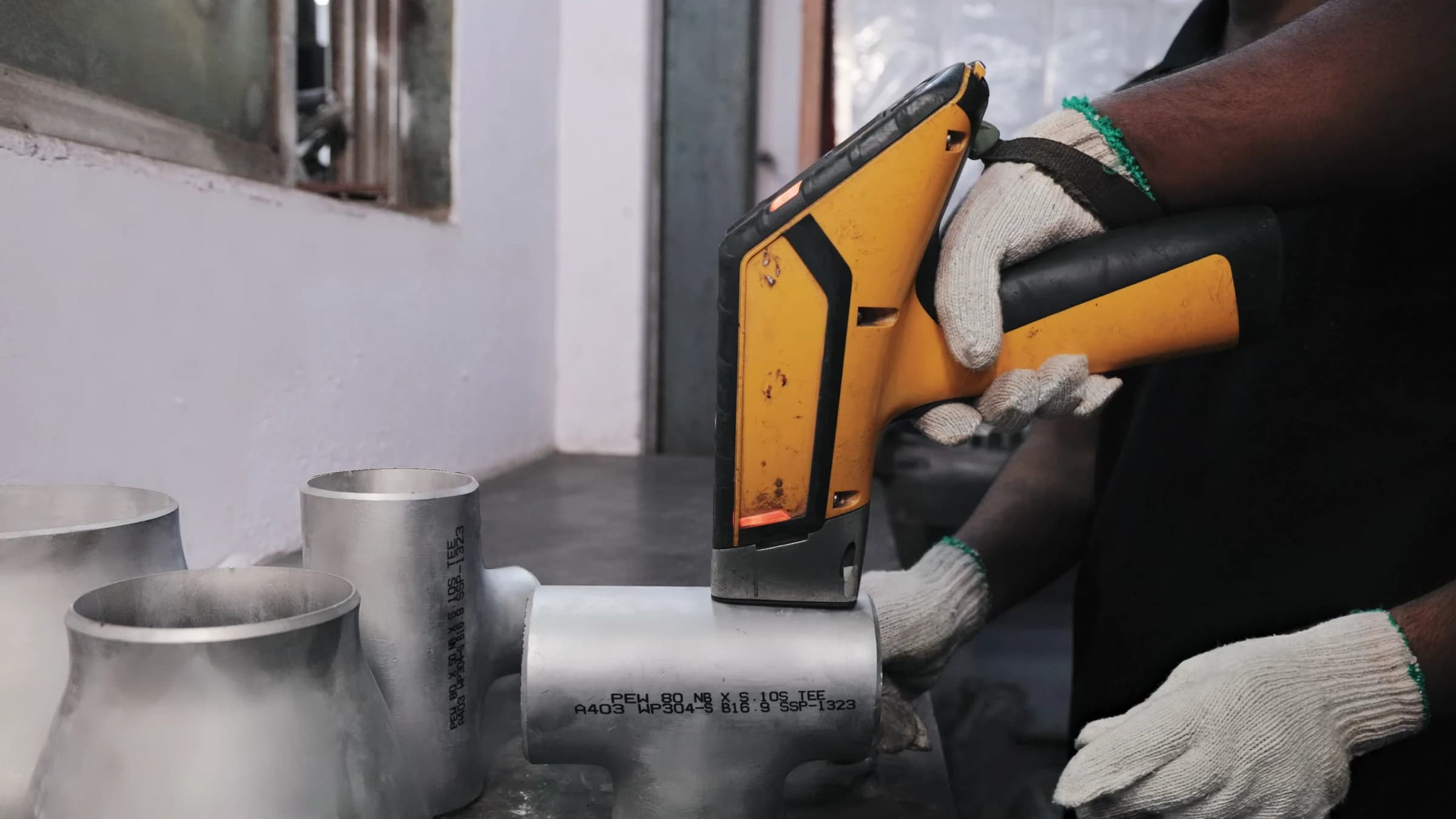 PMI analyser held against a marked stainless-steel tee by gloved hands
