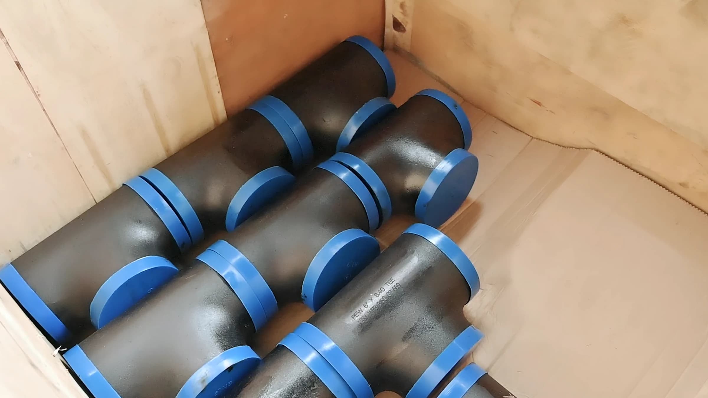 Carbon-steel tees with blue end caps packed in a wooden case for dispatch